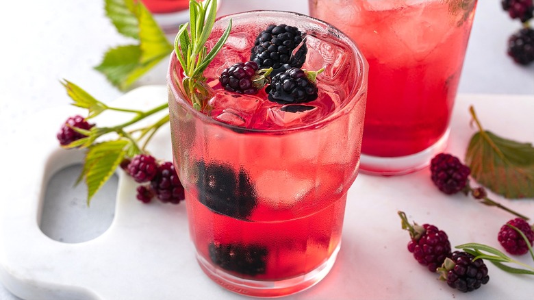 Cocktail teinté de rose avec mûres fraîches, romarin et glace dans un verre transparent.