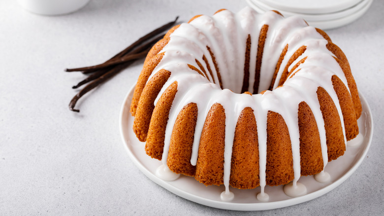 Gâteau Bundt avec glaçage blanc sur une assiette à côté des gousses de vanille