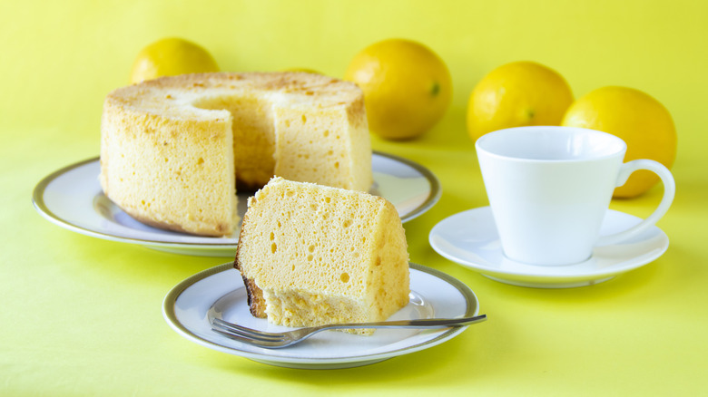 Gâteau en mousseline avec une tranche sur une assiette à côté d'une tasse à café et des citrons en arrière-plan