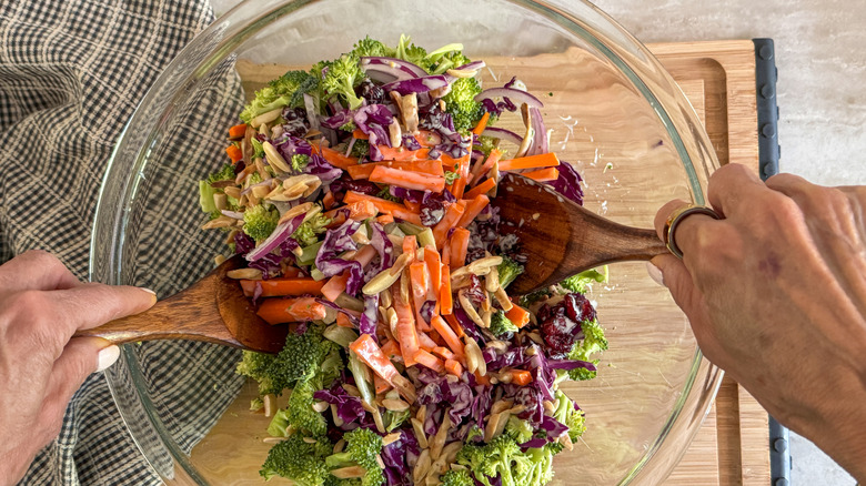Mains utilisant des cuillères en bois pour mélanger la salade de brocoli dans un bol