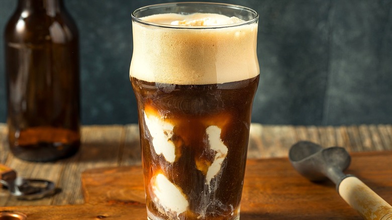 La bière de racine faite maison flotte dans un verre transparent sur une planche de service en bois à côté d'une cuillère à glace