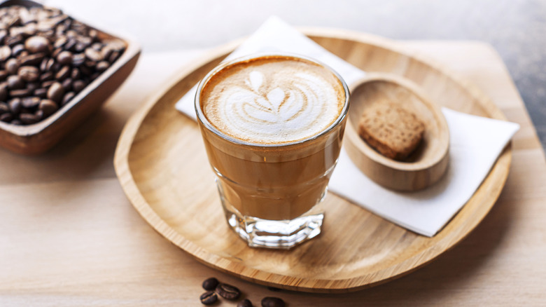 Un café cortado sur un plateau à côté d'un petit biscuit.