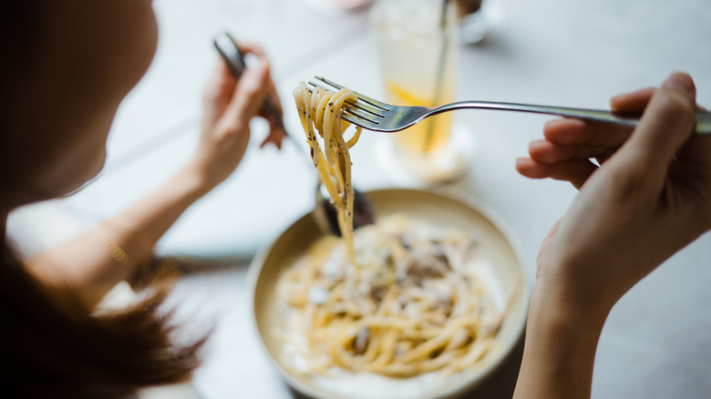 Une femme aime manger un spaghetti carbonara dans un restaurant italien avec une fourchette.