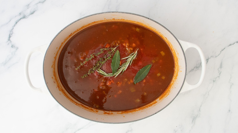 Diverses herbes posées sur la sauce pomodoro dans un four hollandais