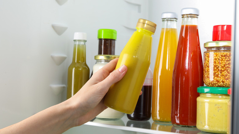 femme sortant une bouteille de moutarde du réfrigérateur