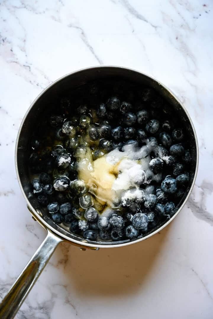 les myrtilles, le sucre, le miel et l'eau dans une casserole avant la cuisson.