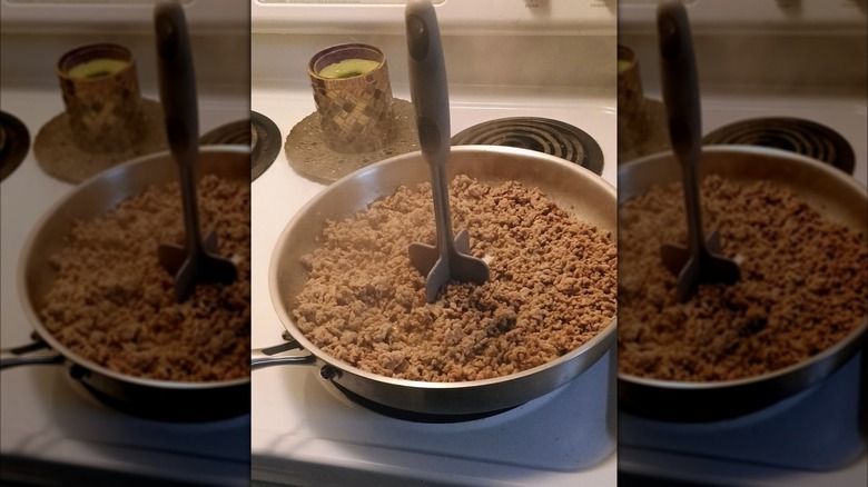 Hachoir à viande debout dans une poêle de bœuf haché sur une cuisinière électrique