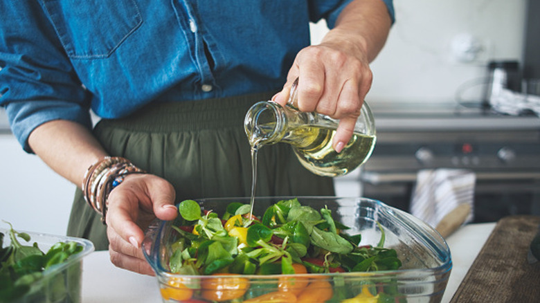 Une femme ajoutant de l’huile d’olive dans une salade.