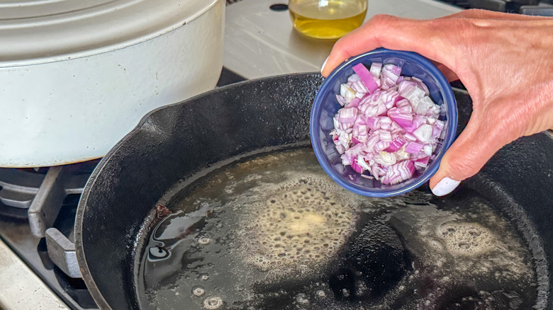 main ajoutant des oignons à la poêle