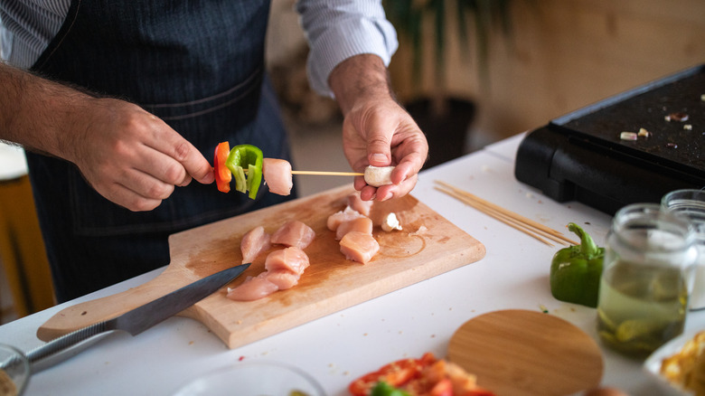 Un chef broche du poulet cru et des légumes
