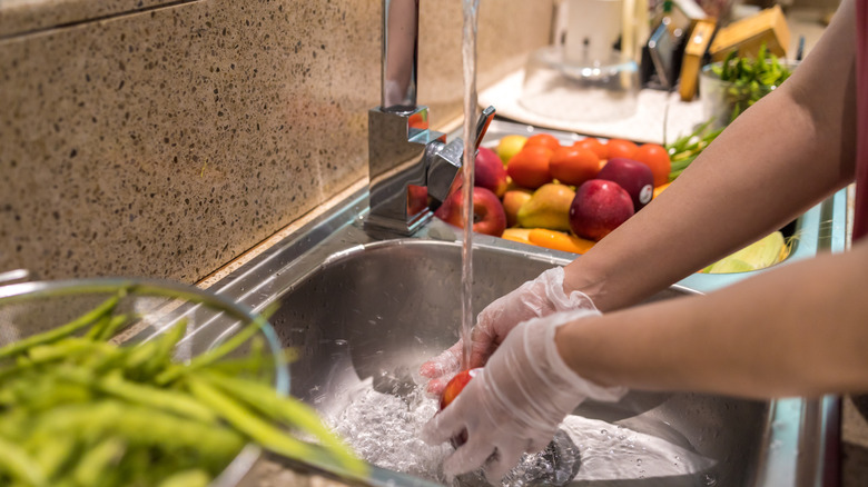 Une femme rinçant des produits frais dans la cuisine.