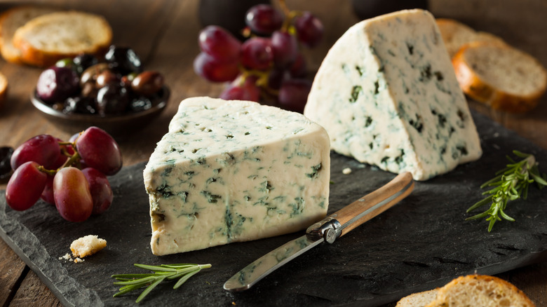 Quartiers de fromage bleu avec raisins et couteau à fromage sur une planche à découper en bois