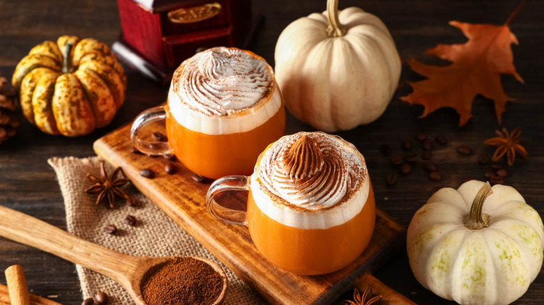 Deux lattés aux épices de citrouille avec crème fouettée sur une planche de bois avec décor d'automne en arrière-plan