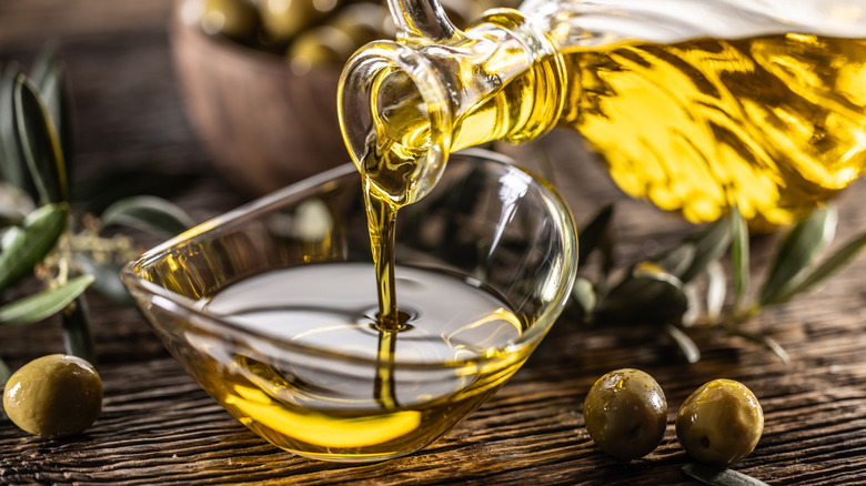 Une bouteille d'huile d'olive est versée dans un petit bol en verre.