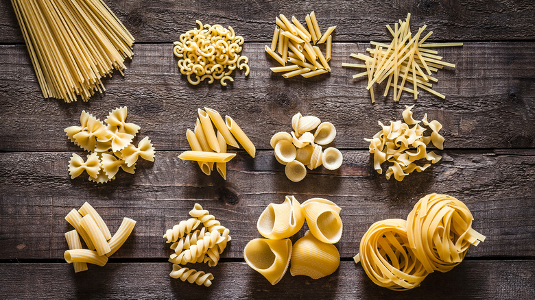 Plusieurs formes de pâtes photographiées du dessus sur une table en bois.