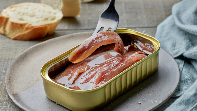 Une fourchette sort un anchois d'une boîte.