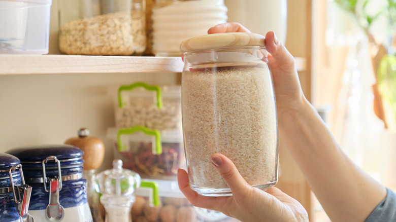 On voit les mains d’une personne tenant un pot de riz en verre.