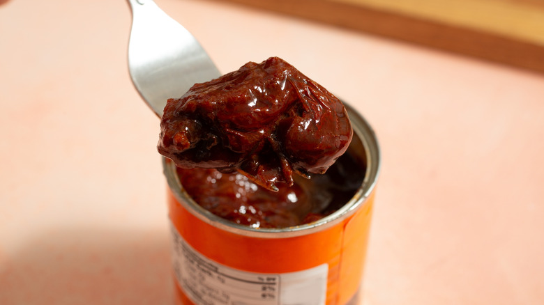Une fourchette retire un poivron d'une boîte de piments chipotle en adobo.