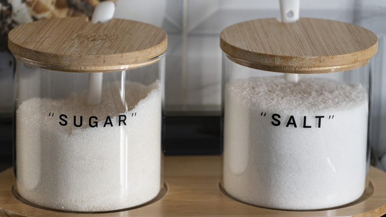 Un grand récipient en verre rempli de sucre à côté d'un autre pour le sel.