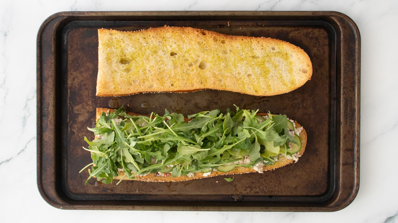 Une salade de thon étagée sur une grosse baguette grillée garnie de bébé roquette