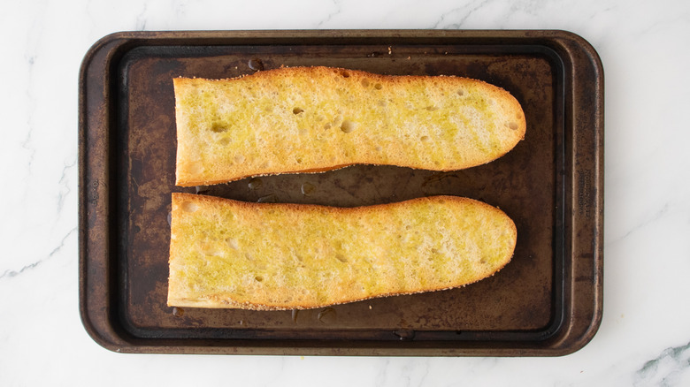 La moitié d'une grosse baguette grillée sur une plaque à pâtisserie