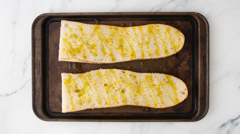 La moitié d'une grosse baguette arrosée d'huile d'olive sur une plaque à pâtisserie.