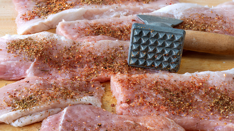 Coupes de viande assaisonnées après avoir été attendries avec un maillet à viande posé sur la planche à découper