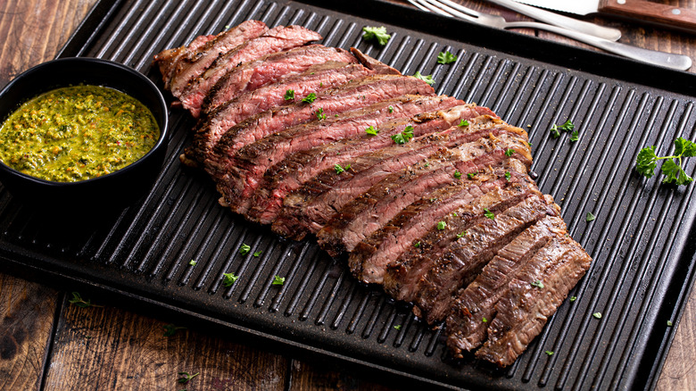 Un gros steak de jupe tranché repose sur un plateau sur une table en bois.