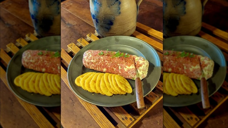 Une bûche de bœuf séchée sur une assiette avec quelques craquelins et un couteau