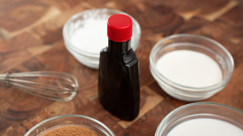 Une bouteille d'extrait de vanille entourée d'autres ingrédients de pâtisserie