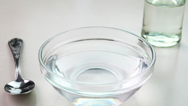 Un bol de vinaigre avec un verre d'eau derrière