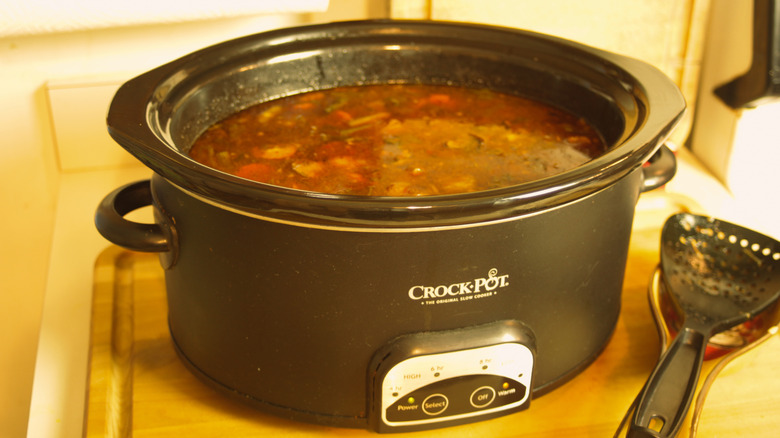 Mijoteuse ovale Crock-Pot avec un ragoût fini à l'intérieur et une spatule sur le comptoir pour remuer.