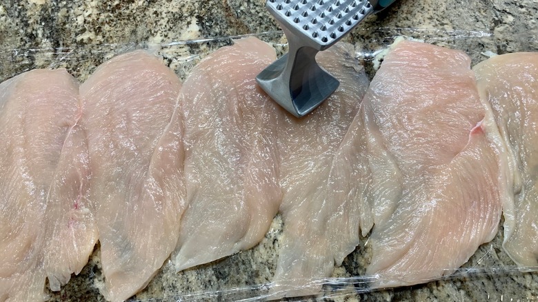 Un cuisinier utilisant un maillet à viande sur un morceau de viande recouvert d'une pellicule plastique