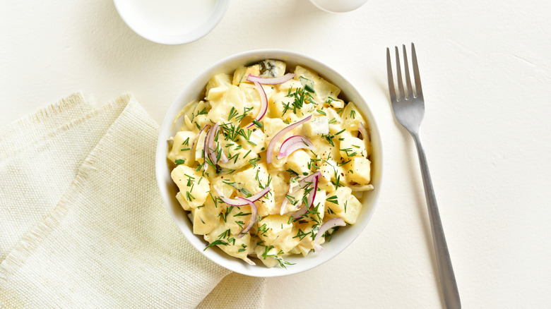 Bol de salade de pommes de terre aux herbes et oignons, une fourchette et une serviette sur le côté