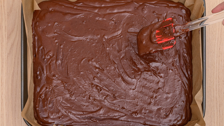 Spatule lissante pâte à brownie versée dans un plat allant au four.