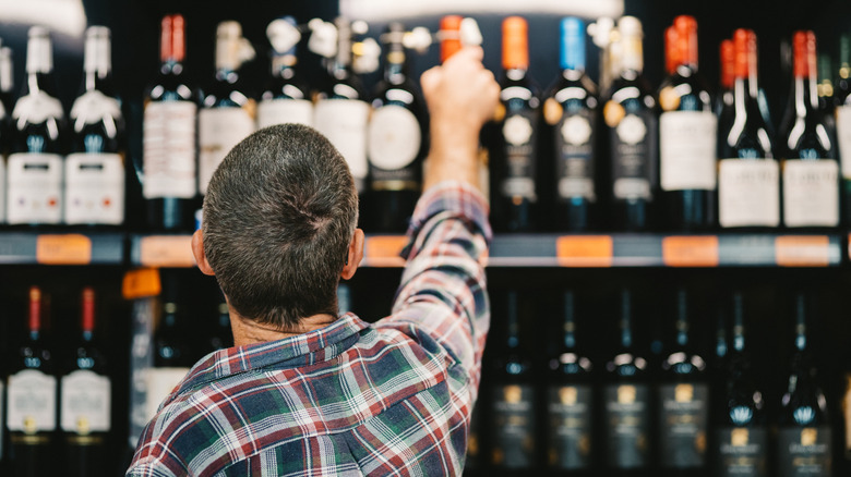 Un homme cherchant une bouteille de vin dans un magasin.