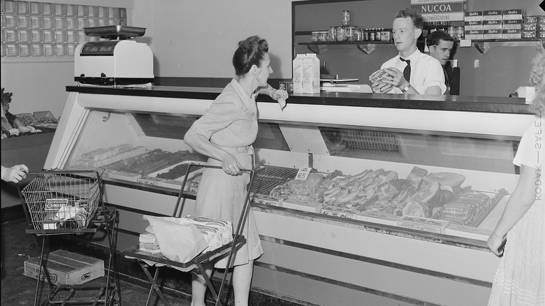 Photo en noir et blanc d’une femme en robe commandant de la viande chez un boucher.
