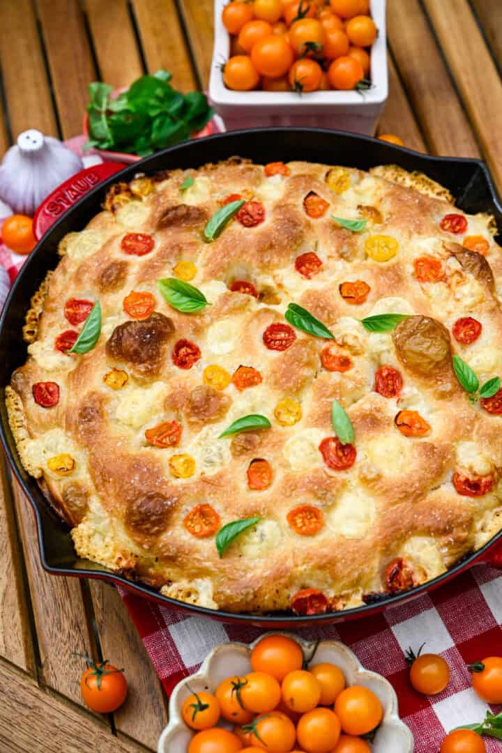 Vue aérienne de la focaccia aux tomates et au basilic dans une poêle en fonte rouge.