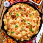 Vue aérienne de la focaccia aux tomates et au basilic dans une poêle en fonte rouge.