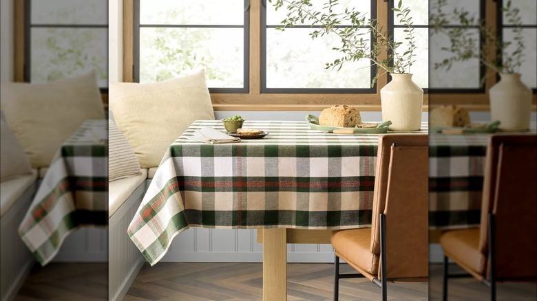 Une nappe à carreaux aux couleurs marron caramel et vert habillant une table en bois avec une chaise derrière elle.