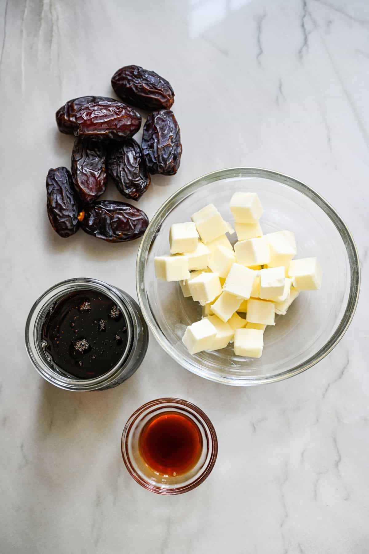 vue aérienne du beurre, des dattes, du sirop d'érable et de l'extrait de vanille pour montrer les ingrédients de la sauce caramel aux dattes.