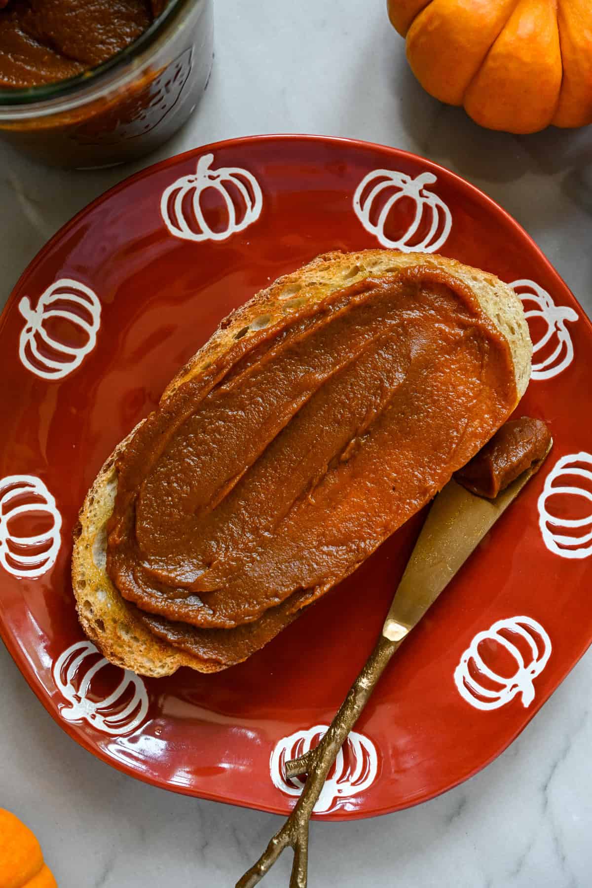 Une tranche de pain grillé badigeonnée de beurre de citrouille maison sur une assiette orange avec des citrouilles sur le pourtour.