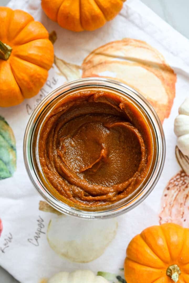 Vue rapprochée d'un pot de beurre de citrouille fait maison sur un linge sur le thème de l'automne à côté de mini citrouilles pour la décoration.