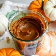 Vue rapprochée d'un pot de beurre de citrouille fait maison sur un linge sur le thème de l'automne à côté de mini citrouilles pour la décoration.