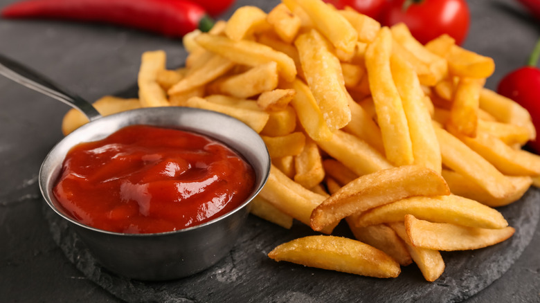 Ramequin de ketchup à côté d'un tas de frites.