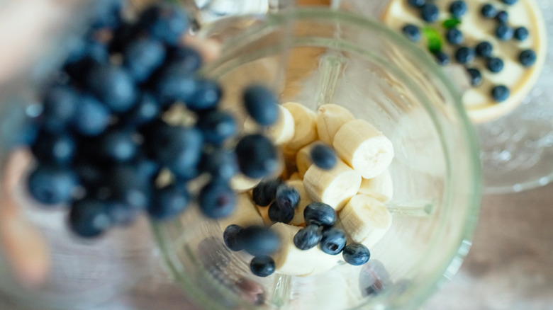 ingrédients du smoothie comme les bananes et les myrtilles entrant dans un mélangeur