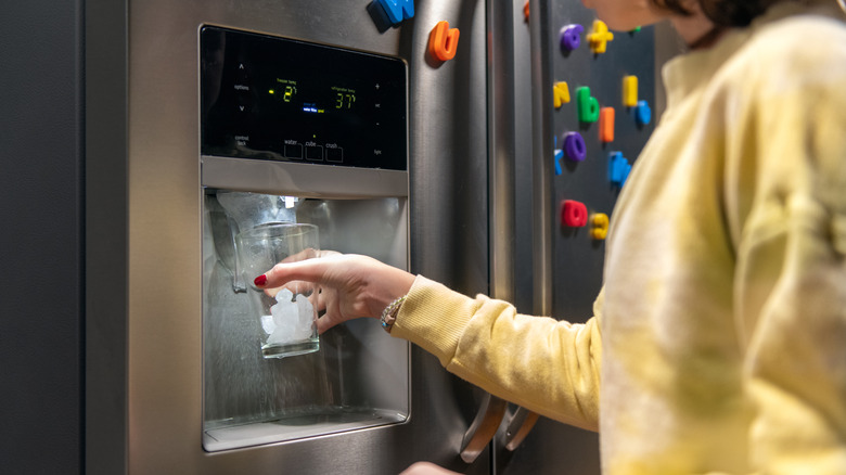 Personne tenant un verre sous une machine à glaçons automatique dans la porte d'un réfrigérateur