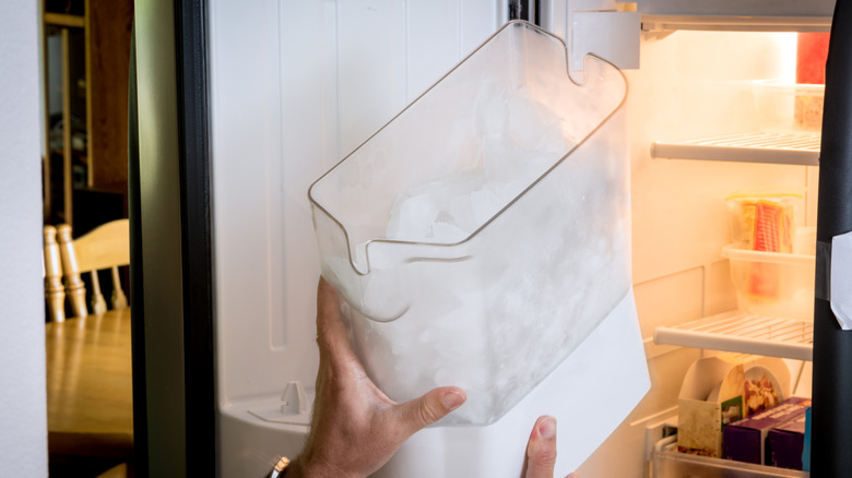 Personne retirant un récipient à glace rempli de glaçons du congélateur