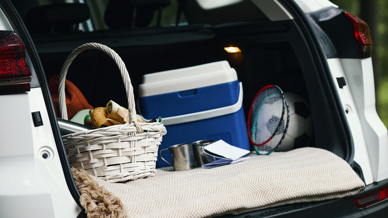 Une glacière dans le coffre avec d'autres accessoires de plein air, comme une raquette de badminton, une couverture de pique-nique et un panier