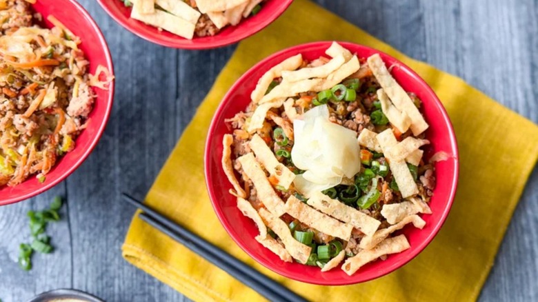 un bol rouge avec du porc haché, des wontons, des oignons verts et d'autres ingrédients d'un rouleau aux œufs de porc
